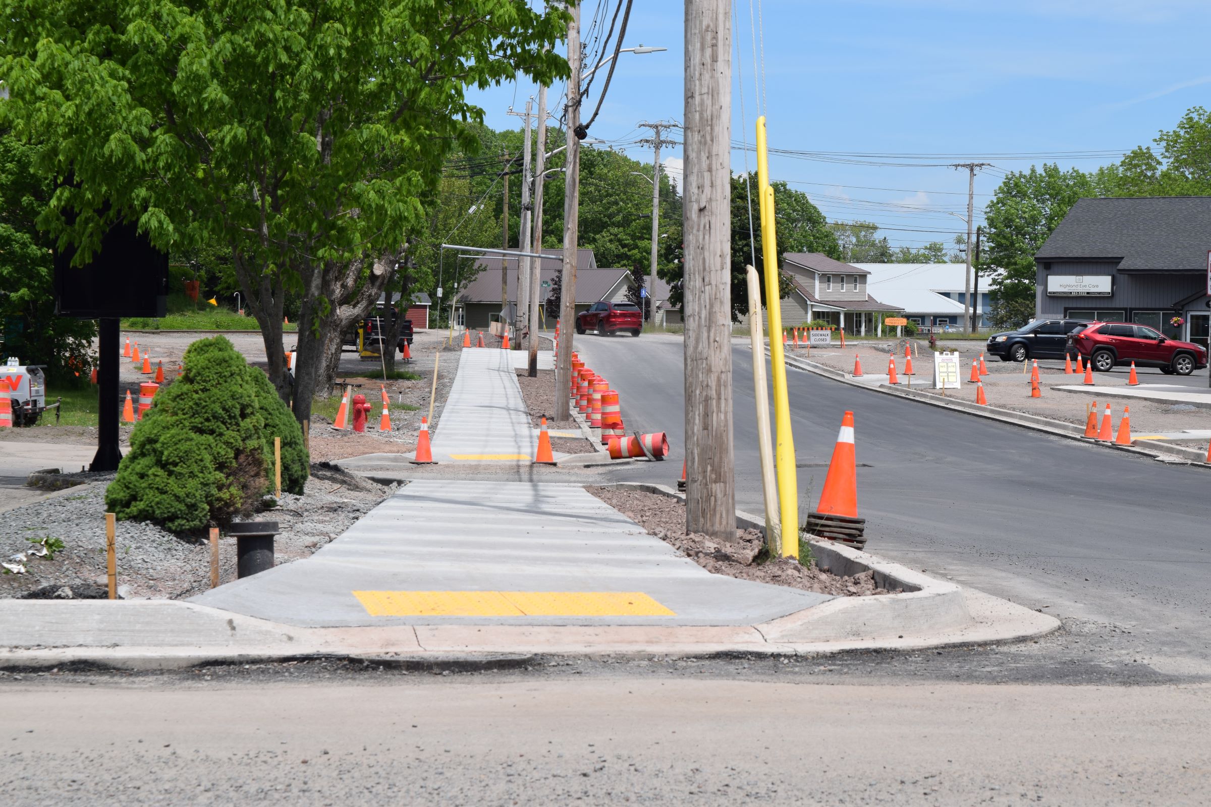 Image depicting ongoing road work in Antigonish, Nova Scotia for the Bay Street Project. Pictured are freshly poured concrete sidwalks, orange pylons, some cars on the street.